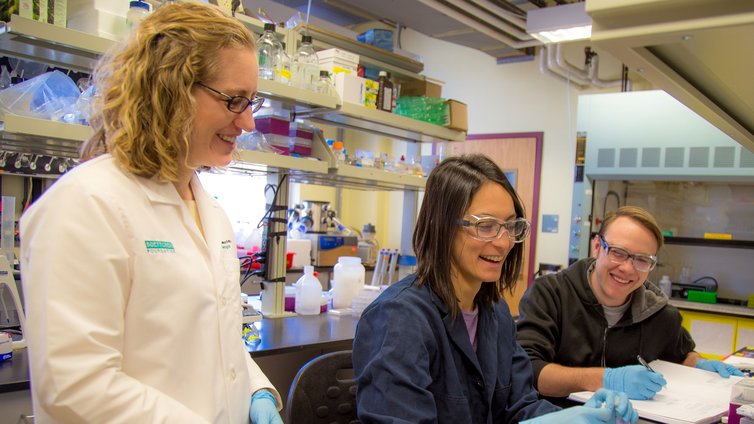 Three chemical engineers in a laboratory with equipment and paperwork