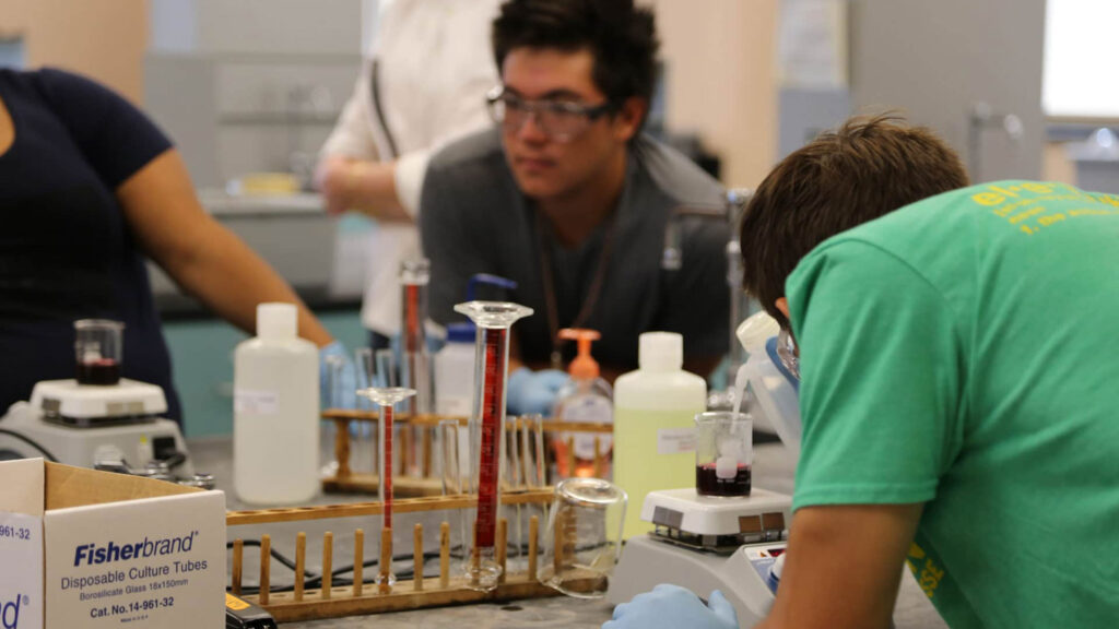 chemists working in a lab setting with test tubes and chemicals on the lab table