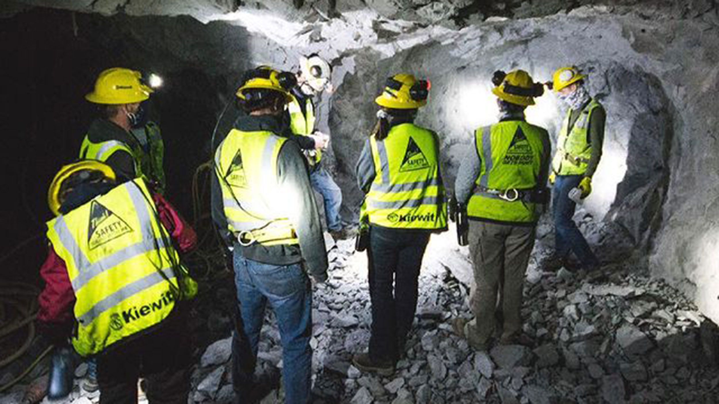 Mining engineers wearing helmets and reflective vests working together inside a mine