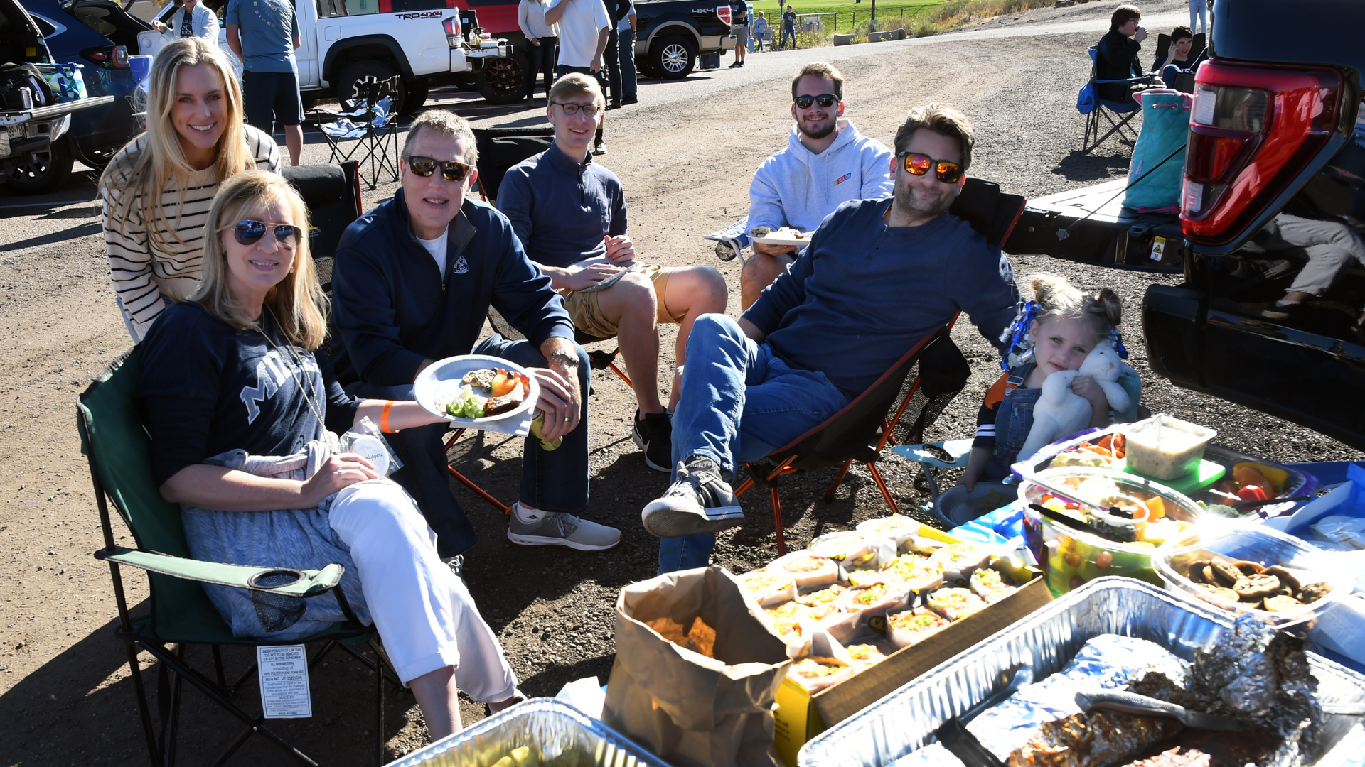 several family members and students gather around a tailgating spread