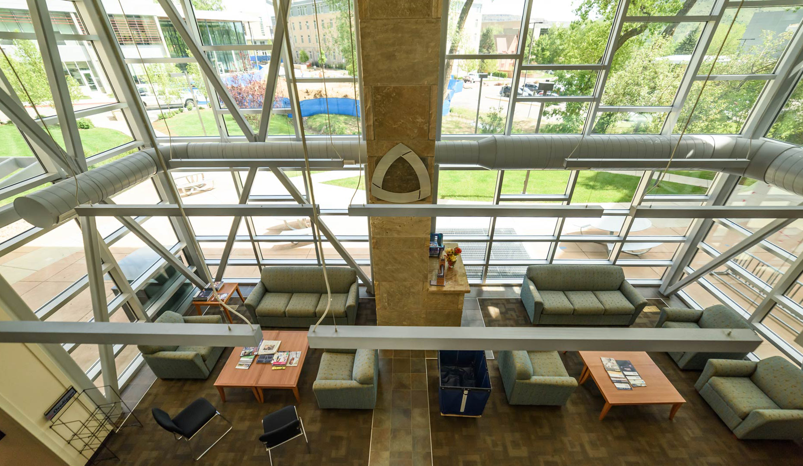 Interior with high glass walls and seating in a lobby, mines logo on wall, outside green grass and ttrees